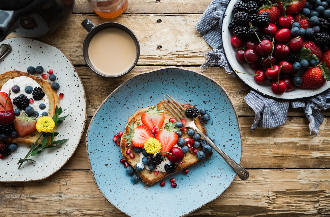 A table with a breakfast: red fruits, a toast with iogurt and red fruits, pancakes and a coffee