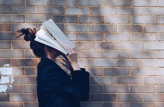 a girl covering hher face with a book, trying to concentrate